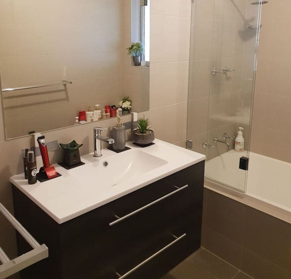 Completed bathroom renovation with full height tiled walls, a glass screened shower over bath, and a floating dark timber vanity