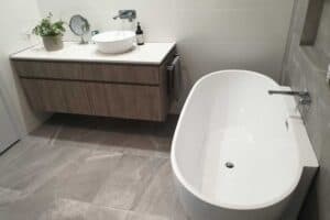 Bathroom fit out with a floating timber look vanity, round vessel basin and freestanding bath on tiled flooring