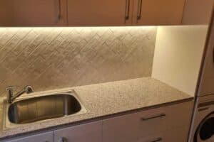Herringbone pattern kitchen splashback tiling shown close up under cabinet lighting