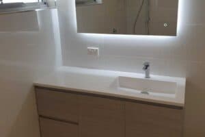 Bathroom vanity under a backlit LED mirror, set against subway tiled walls